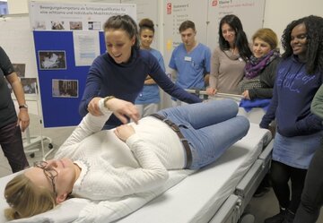 Auszubildende und examinierte Pflegekräfte üben, wie man Patienten aktiv in Umlagerungen einbezieht.