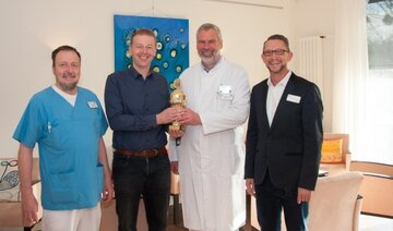 Symbolische Übergabe auf der Palliativstation mittels Pokal der Tipprunde: der pflegerische Teamleiter Klaus-Peter Denia, Tippspielleiter Marc Ruppin, der Leitende Arzt Dr. med. Markus Sosada sowie Dr. rer. nat. Thomas Vorwerk, Leiter der Zentralapotheke