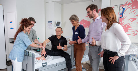 Edmund Steigerwald ist der erste Patient auf der Station C5 im KRH Klinikum Siloah mit dem neuen Armband vom Projekt Infection Control System (ICS). Von links: Cansu Bagiran, Pflegefachkraft auf der C5, Kathleen Linke, Stationsleitung der C5, Dr. Karin Kobusch, Leitende Oberärztin Krankenhaushygiene des Instituts für Medizinische Mikrobiologie und Krankenhaushygiene, Daniel Ewert-Schönstein, Senior IT-Projektmanager Krankenhausdigitalisierung und Elisa Kroczek, Siemens Healthineers.