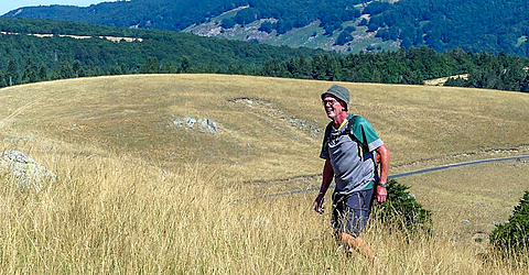 Peter Fricke ist Wandern und läuft auf einer Wiese. Die Sonne scheint und er trägt einen Hut