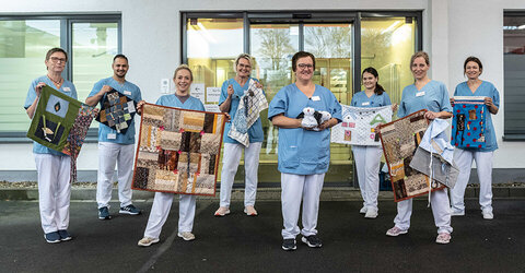 Freuen sich für ihre Patientinnen und Patienten: Pflegekräfte des KRH Klinikum Robert Koch Gehrden mit den gespendeten Nesteldecken sowie den aus Handtüchern gefalteten Hundefiguren.