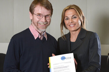 Michaela Noll überreicht Dr. Michael Schneider das Zertifikat „Ausgezeichnet. FÜR KINDER“.