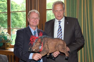 Bürgermeister Jörg-Roger Hische (rechts) überreicht dem Kaufmännischen Direktor  Wolfgang Grotstück einen Miniatur-Keiler