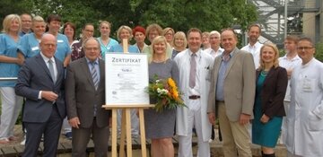 Übergabe im Klinikpark: Dr. Martin Memming (links) und Marit Neels (Mitte) nehmen stellvertretend für alle Beschäftigten des Klinikums Neustadt am Rübenberge das Zertifikat entgegen.