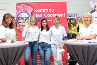 Mitarbeiterinnen stehen vor Plakaten am Stand