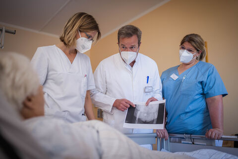 Auf Station stehen Stationsärztin Mirja Schraverus-Meuer, Stationsleiterin Stephanie Robertson und Pflegefachkraft vor dem Patientenbett 